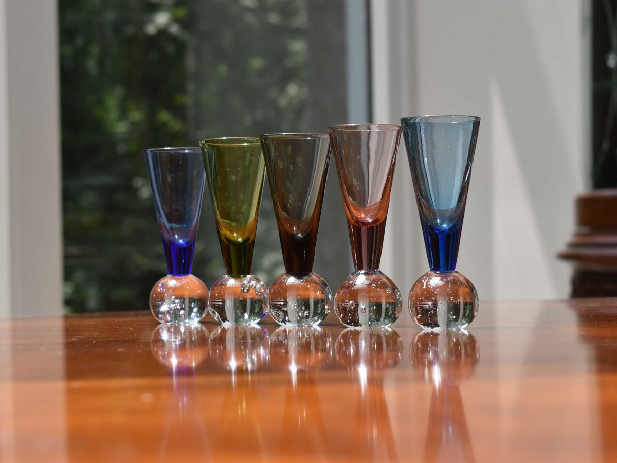 Five coloured cordial glasses with bubble stems on the Convivial table